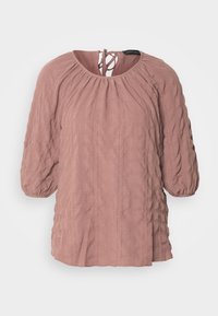 Blouse texturée mauve clair avec encolure froncée, manches bouffantes trois-quarts et fermeture à nouer au dos.
