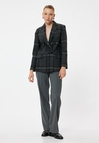 Blazer de cuadros gris de doble breasted con solapas pronunciadas, bolsillos frontales y detalles de botones, combinado con pantalones grises a medida y zapatos negros.