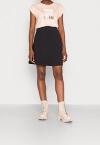 Camiseta de color rosa claro con un estampado gráfico, combinada con una falda negra de corte acampanado y botines de cordones beige. Un atuendo simple y casual.