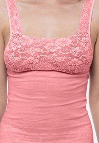 Pink tank top with a lace overlay at the neckline, featuring a square design and fitted body. Smooth texture with adjustable straps.