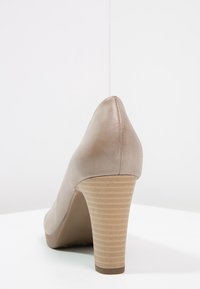 Escarpin beige à talon haut avec un bout pointu, texture en cuir lisse et un design de talon en bois nervuré. La semelle est d'une couleur brun clair unie.