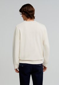 Crème sweatshirt met een ronde hals en ribgebreide manchetten, gecombineerd met donkere broeken met zijzakken en zichtbare stikseldetails.