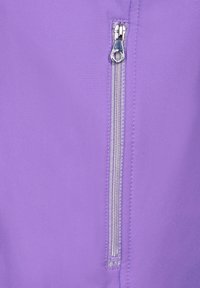 Lila jacka med en silverdragkedja med dragflik, mjukt material och sydda detaljer längs dragkedjan.