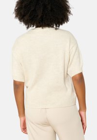 Cream-colored knit sweater with short sleeves and a relaxed fit. Soft texture with a ribbed hem and cuffs. No visible patterns or accents.
