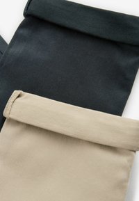 Baumwollhosen in Schwarz und Beige mit umgeschlagenen Säumen. Glatte Textur mit leichtem Glanz auf dem schwarzen Stoff und matter Oberfläche auf dem beigen.