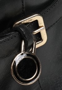 Szczegół czarnego skórzanego paska z złotą metalową klamrą i okrągłym czarnym akcentem. Powierzchnia jest gładka z delikatnym połyskiem.