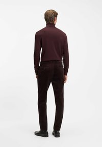 Bordeauxrode coltrui gecombineerd met donkerbruine ribfluwelen broek. De broek heeft achterzakken met knopen en een gladde textuur.