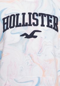 Bluza Hollister w kolorze białym z marmurkowym wzorem w pastelowych odcieniach różu, niebieskiego i pomarańczowego. Posiada granatowe, wyszywane logo i wzór ptaka.