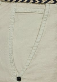 Béžové látkové kalhoty s texturovaným povrchem, které mají přední kapsu, kontrastní šití a splétaný námořnický pas.