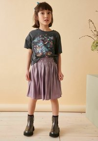 Grå t-shirt med färggårdstryckt design, tillsammans med en lavendelfärgad kjol med rynkad midja och svarta läderankelstövlar.