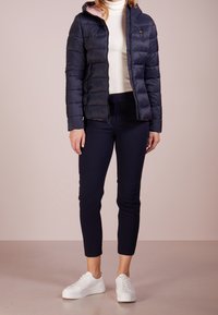Giubbotto imbottito blu navy con cuciture orizzontali, cappuccio e fodera rosa; abbinato a pantaloni neri aderenti e sneaker bianche.