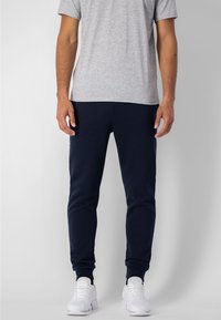 Pantalones jogger azul marino, diseño ajustado con puños elásticos, combinados con una camiseta gris claro y zapatillas blancas. Textura de tela suave.