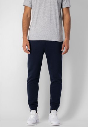 Pantalones jogger azul marino, diseño ajustado con puños elásticos, combinados con una camiseta gris claro y zapatillas blancas. Textura de tela suave.
