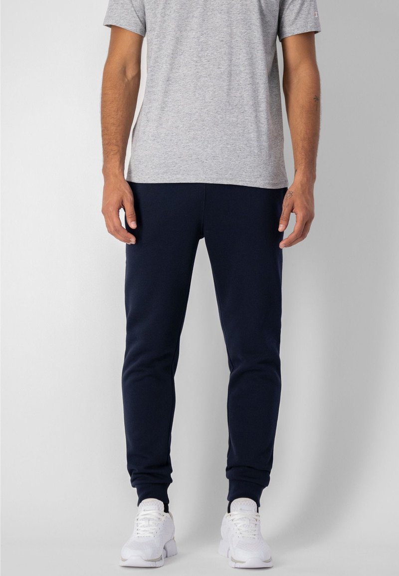 Pantalones jogger azul marino, diseño ajustado con puños elásticos, combinados con una camiseta gris claro y zapatillas blancas. Textura de tela suave.