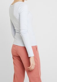 Ljusblå ribbad långärmad topp, figursydd design med rund halsringning och subtil textur, kombinerad med rosa sweatpants.