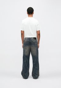 Ohlapne kavbojke iz jeansa z zbledelim modrim pranim, z velikimi žepi in subtilnimi detajli našivanja, kombinirane z navadno belo majico.