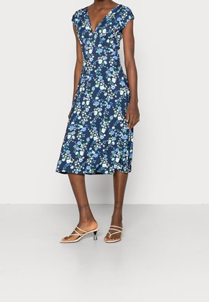 Robe florale marine avec un décolleté en V, des manches courtes, et une longueur midi. Présente des motifs floraux blancs et bleus. Associée à des talons beiges à lanières.
