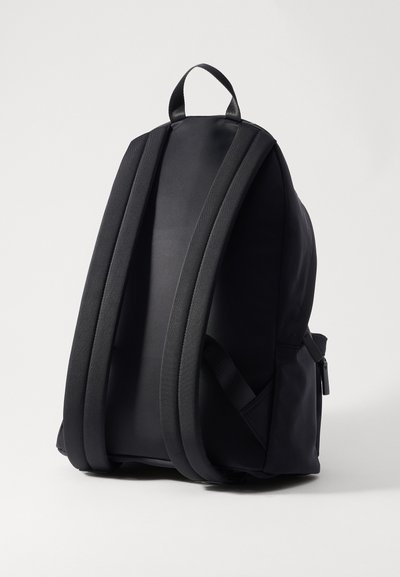 Sac à dos noir avec des bretelles et un panneau arrière rembourrés. Fabriqué à partir d'un matériau durable, il dispose d'une poignée supérieure et de poches latérales pour le rangement.