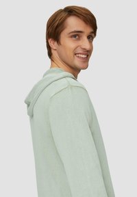 Lichtgroene hoodie met een ontspannen pasvorm, textuurstof en een capuchon met trekkoord. Voorzien van ribgebreide manchetten en zoom, weergegeven vanuit de zijkant.