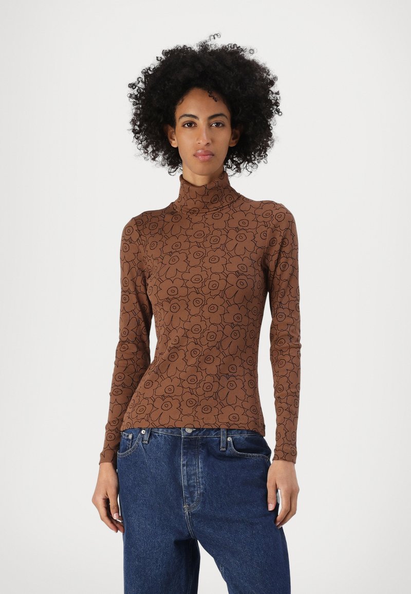 Brauner langärmeliger Rollkragenpullover mit schwarz floralem Muster. Figurbetonter Schnitt, weiche Textur, getragen mit hochgeschnittenen blauen Jeans.
