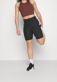 Pantalones cortos deportivos negros con una cintura alta y un diseño ajustado, combinados con un top corto marrón. El conjunto incluye un bolsillo lateral.