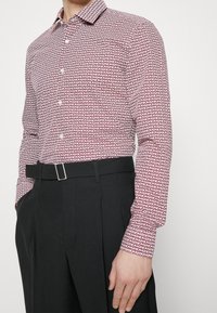 Punavalkokuvioitu pitkähihaisen paidan, jossa on napillinen kaulus, yhdistelty mustiin laskostettuihin housuihin ja hopeanväriseen vyönsolkeen.