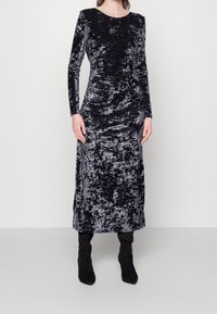 Robe en velours noir à manches longues, col rond, corsage ajusté et jupe maxi droite. Texture remarquable avec un léger éclat.