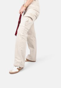 Beige Cargo-Hosen mit Seitentaschen, lässiger Schnitt und leichter Denim-Textur, kombiniert mit Sneakers mit einem Leopardenmuster.