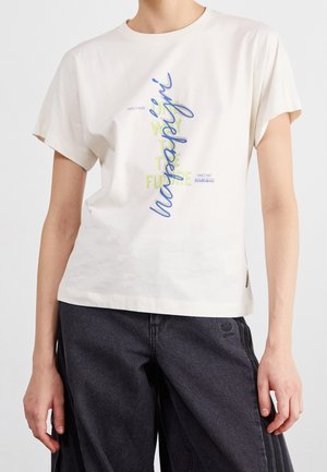 Personne portant un t-shirt blanc avec un texte bleu et jaune "Happiness" et "Expect more" assorti à un pantalon foncé.