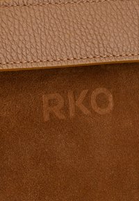 Bolso de cuero marrón con una superficie texturada y granulada, y una correa de cuero suave con costuras. Detalle en relieve de "RKO" visible en la gamuza.