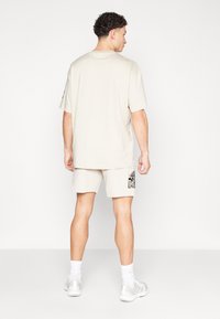 T-shirt bege oversize com mangas curtas, combinada com calções a condizer que apresentam uma estampa gráfica escura na coxa esquerda.