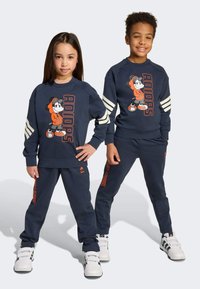 Marineblauwe sweats en broeken voor kinderen, met een cartoonfiguur ontwerp. Witte strepen op de mouwen. Materiaal lijkt zacht en textuurrijk.