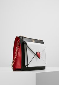 Borsa strutturata bianca e nera con accento di cuore rosso, hardware dorato e tracolla a catena. Interno rosso. Design a busta.