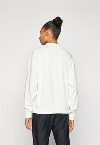 Felpa bianca con un taglio rilassato, spalle abbassate e polsini a coste. Texture morbida; design semplice e minimalista senza fantasie.