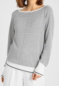 Sweter dzianinowy w czarno-białe paski z szerokim dekoltem, prążkowanymi mankietami oraz teksturowanym szwem centralnym, charakteryzujący się luźnym krojem.