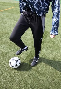 Black athletic pants with gray accents, paired with black soccer cleats, engaged with a black and white soccer ball on green turf.
