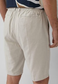 Helle beige Shorts aus einem strukturierten Stoff, mit einem elastischen Bund, zwei Gesäßtaschen und einem kleinen Logodetail.