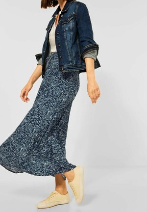 Veste en jean, haut blanc et une longue jupe bleue à motifs avec une silhouette fluide, assortis à des baskets jaune clair.