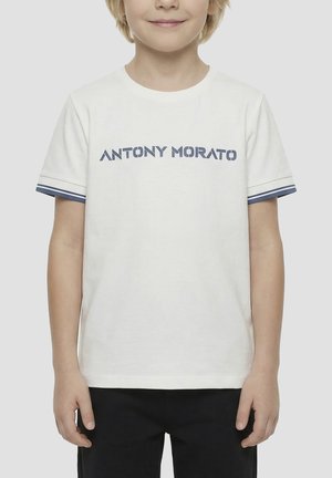 Bambino che indossa una t-shirt bianca a maniche corte con la scritta "ANTONY MORATO" stampata in blu e bordi a righe sulle maniche.