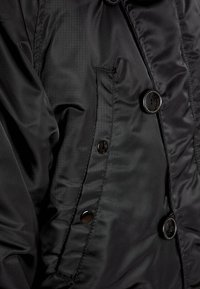 Schwarze Steppjacke mit glatter, glänzender Oberfläche, doppelreihigem Design und schwarzen Kunststoffknöpfen sowie seitlicher Taschenapplikation.