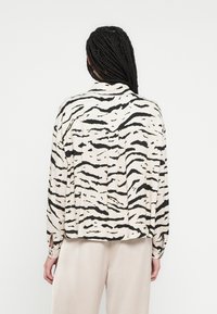 Blouse à manches longues et col en crème avec des rayures de tigre noires. Présente une coupe décontractée, des poignets à boutons et un ourlet légèrement arrondi.