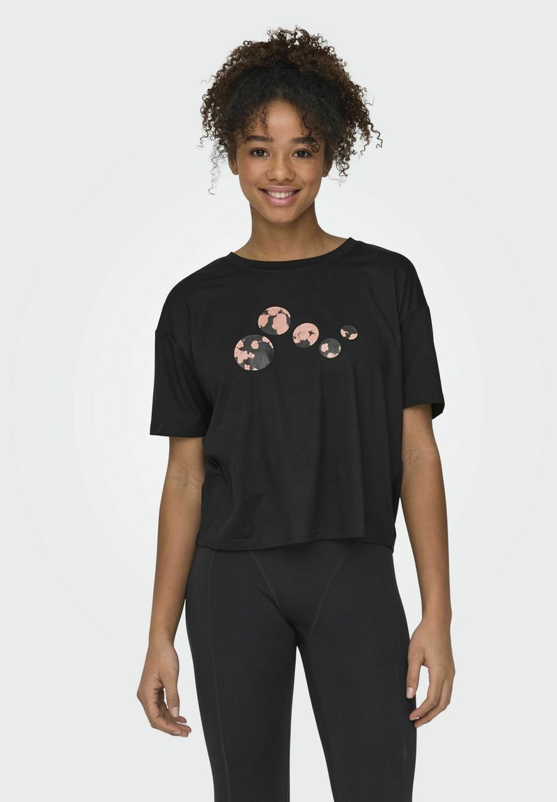 Camiseta corta negra con mangas cortas, que presenta un gráfico de círculos superpuestos en rosa y gris. Textura de tela suave.