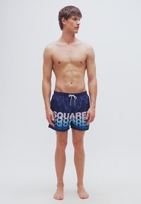 Μπλε σκούρες βερμούδες για κολύμβηση με γραφικό κείμενο "SQUARE" σε βαθμιαία διαβάθμιση σε ανοιχτό ροζ και μπλε. Διαθέτουν ελαστική μέση και κορδόνι ρύθμισης.