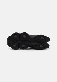 Black sneaker sole featuring a textured rubber surface with a diamond pattern, ridges, and support elements for traction and durability.