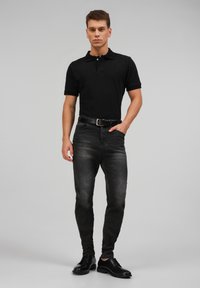 Crna polo majica, uske tamno sive traperice i crne cipele za odijelo. Elegantna dizajn s glatkom teksturom i minimalnim detaljima.