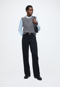 Szary wełniany bezrękawnik na jasnoniebieskiej koszuli, czarne spodnie o prostych nogawkach i czarne obuwie, charakteryzujące się prostym wzorem i czystymi liniami.