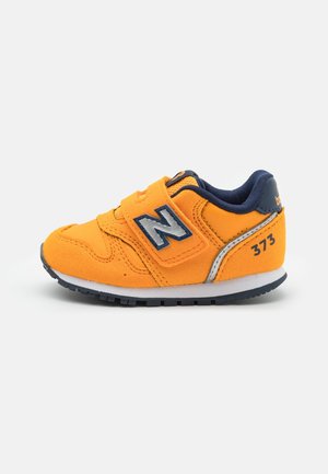 Jasnopomarańczowy but sportowy dla malucha z granatowymi akcentami, paskiem na rzep, białą podeszwą i logo "N" po boku, numer modelu 373 na pięcie.