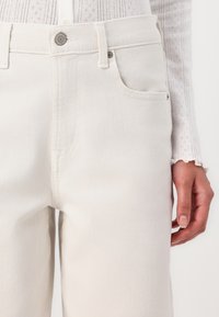 Vita denimjeans med en lätt textur, femfickorsdesign, metalldknappsstängning och subtila sömdetaljer. Skräddarsydd passform vid midjan.