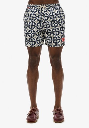 Bañador azul marino con un patrón floral blanco, cinturilla elástica, cordón de ajuste y detalle del logo rojo en la pierna izquierda.