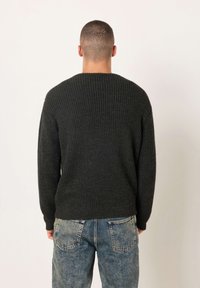 Tamnosivi džemper rebraste teksture s dugim rukavima i okruglim izrezom, uparen s izblijedjelim plavim trapericama. Teksturirani materijal vidljiv je na stražnjoj strani.